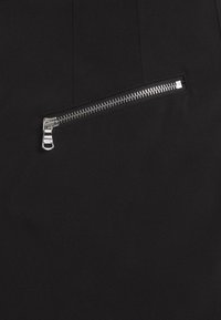 Un tissu noir présente une texture lisse avec une poche zippée en argent proéminente. La fermeture éclair a une finition métallique et est placée au centre sous la couture.
