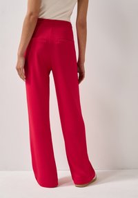 Rode, structuurwijde broek met zakken, met een hoge taille en een gladde afwerking. De achterzijde toont stikseldetails en subtiele accenten.