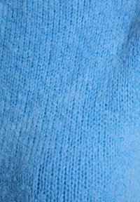 Tessuto di maglia azzurro chiaro con una texture morbida, che mostra un motivo uniforme e filamenti sottili, creando un aspetto caldo e accogliente.
