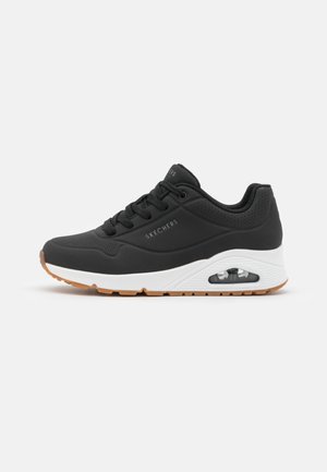 Czarny sneaker Skechers z białą wyściełaną podeszwą, widoczną poduszką powietrzną, sznurowaniem z przodu i brązową gumową podeszwą zewnętrzną, widok z boku na białym tle.