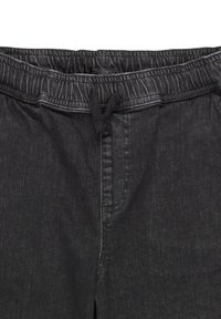 Mustat denimi-housut, joissa on joustava vyötärö ja musta nyöri etuosassa.