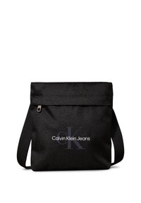 Sort stof skuldertas med lynlåslukning. Har et fladt design og trykt "Calvin Klein Jeans" logo i hvid og grå.