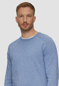 Jasnoniebieski sweter z okrągłym dekoltem, wykonany z teksturowanej tkaniny, z długimi rękawami i miękkim, dzianinowym wzorem. Posiada kontrastowy biały kołnierzyk.