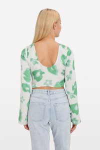 Dlhý rukáv, crop top v bielej farbe s zelenou kvetinovou potlačou. Má hlboký výstrih na chrbte a textúrovanú látku, v kombinácii so svetlomodrými džínsami.