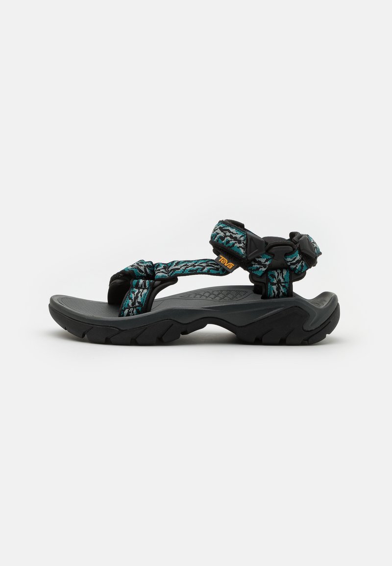 Sandales noires avec des brides tissées teal et noires, boucle ajustable et semelle grise texturée. Conçues pour la durabilité et le confort.