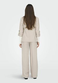 Blazer beige su misura con maniche arrotolate e pantaloni a gamba larga abbinati. Tessuto liscio, design semplice e dettagli minimi.