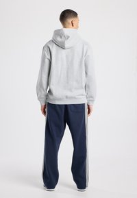 Grijze hoodie met een losse pasvorm, gecombineerd met marineblauwe trainingsbroek met witte strepen langs de zijkant. De textuur is zacht en glad.