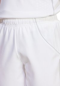 Weiße Sportbekleidung mit elastischem Bund, das eine subtile, strukturierte Musterung und ein schlankes Design aufweist, von der Taille abwärts gezeigt.