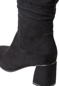 Botte haute jusqu'au genou en suède noir avec un bout carré et un talon bloc. Présente une texture plissée et des détails de couture subtils.