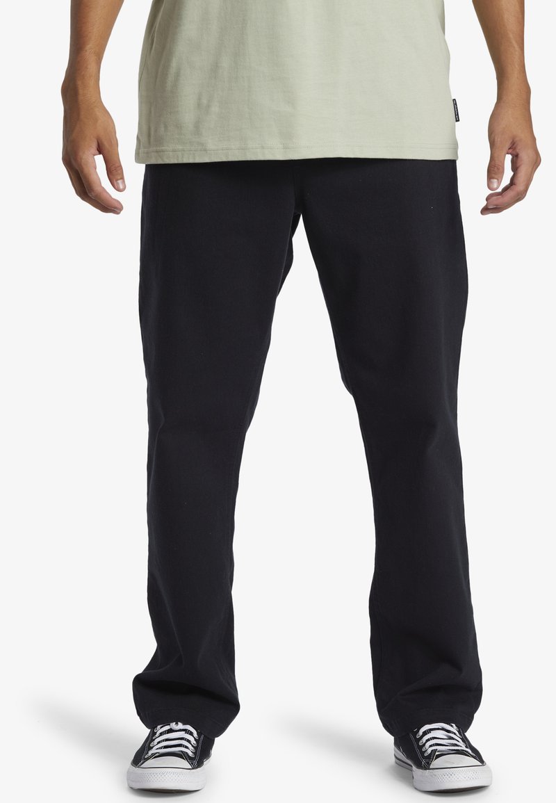 Pantaloni negri din bumbac cu o croială relaxată și picioare drepte, având tocuri pentru curea și buzunare laterale, purtați cu adidași negri.