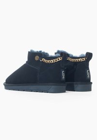 Botines tobilleros azul marino con forro de piel suave, material de ante, acento de cadena dorada, logo en el costado y suela texturizada para mayor agarre.