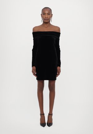Abito nero in velluto con spalle scoperte, maniche lunghe, design aderente e texture morbida, abbinato a tacchi a punta neri.