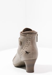 Kožené kotníkové boty v jemném taupe s texturovaným povrchem, ozdobnými hřebíky a nízkým podpatkem. Na vnější straně se nachází logo koně.
