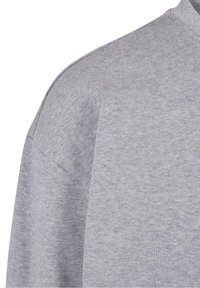 Sudadera gris con un patrón de punto texturizado; cuenta con un cuello redondo y un diseño de hombros caídos para un ajuste relajado.
