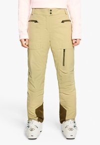 Beige ski pants with a zippered pocket design, featuring a textured lower accent in brown, paired with white ski boots.