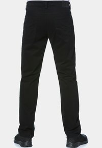 Schwarze Denim-Jeans mit geradem Bein, ausgestattet mit zwei Gesäßtaschen und dezenten Nähten. Getragen mit schwarzen Sportschuhen.