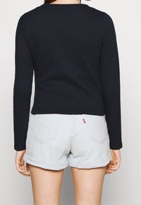 Musta tekstuuri pitkähihaine paita, jossa on pyöreä kaula-aukko, yhdistettynä vaaleansinisiin käännettyihin denim-shortsseihin, joissa on takataskut ja logo-tagi.