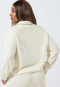 Felpa color crema con vestibilità rilassata, texture morbida e maniche lunghe. Presenta un colletto e polsini a costine.