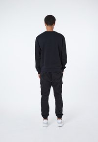 Sudadera negra de manga larga, cuello redondo y puños acanalados, combinada con pantalones cargo negros con bolsillos laterales y puños elásticos.