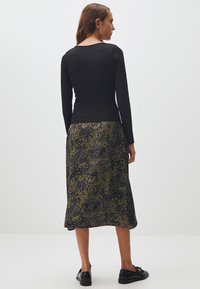 Zwarte geribbelde langemouwen top gecombineerd met een middellange rok met een groen en grijs dierenprintpatroon. Zwarte schoenen met een subtiele glans.