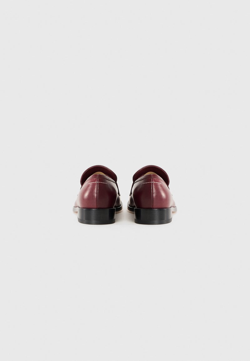 Burgundy läderskor med låg klack, rund tå och sidoutskärningar. Har sömnadsdetaljer och slät yta.