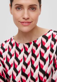 Haut à motif présentant un design audacieux de rayures en chevron rouge, rose et noir. Tissu léger avec une texture lisse et un col large.