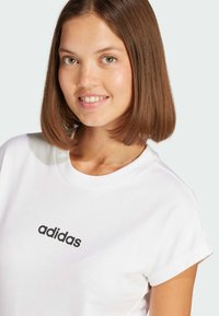 White cotton t-shirt featuring a black "adidas" logo on the front. The shirt has a round neckline and short sleeves.