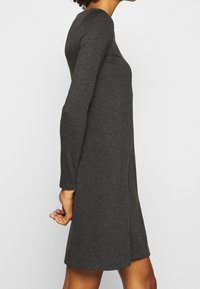 Grå långärmad klänning med åtsittande liv och kjol med volang, tillverkad av mjukt tyg. Har en rund halsringning och minimala sömmar.