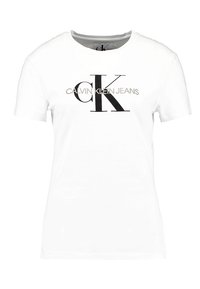 Vit bomullströja med en stor svart "CK"-logotyp och texten "CALVIN KLEIN JEANS" i grått under logotypen. Korta ärmar, rund halsringning.
