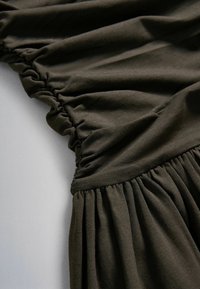 Tissu vert olive foncé avec des coutures élastiques froncées créant des détails de texture plissée et froncée sur un vêtement.