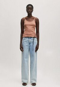 Braunes Tanktop mit dünnen Trägern, kombiniert mit hellblauen weiten Jeans mit Kordelzug. Das Model steht vor einem neutralen Hintergrund.