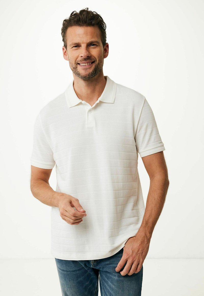 Witte polo met subtiele horizontale strepen, korte mouwen en een kraag. Gekenmerkt door een relaxte pasvorm en textuur, gedragen met blauwe jeans.