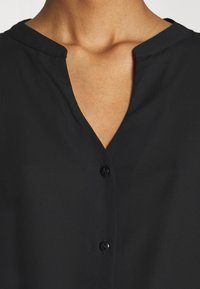 Black blouse with a V-neckline, short collar, and front buttons. Made of smooth fabric with a slight sheen. No visible patterns or accents.