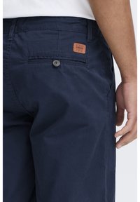 Navy blue shorts made of cotton with a smooth texture, featuring a rear pocket with a button and a leather logo patch.