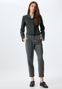 Grijze maatwerk blazer met scherpe revers en bijpassende hoogwaistbroek. Gestructureerde stof met een gladde afwerking, aangevuld met zwarte loafers.