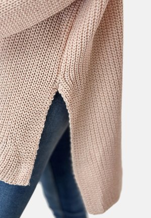 Suéter de punto en suave color rosa con un corte holgado, que presenta una abertura lateral y un tejido texturizado, combinado con denim oscuro.