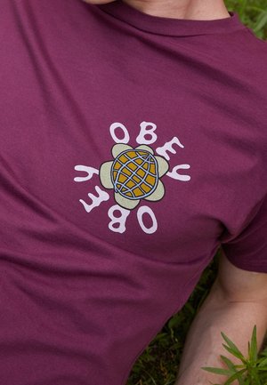 Maroon cotton t-shirt featuring a graphic design with the text "OBEY" surrounding a stylized turtle shell pattern in yellow and blue.