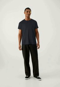 T-shirt de algodão azul-marinho com mangas curtas, combinado com calças largas pretas e ténis pretos. Personagem a usar óculos de sol amarelos.