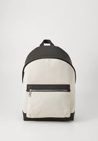 Backpack in cream and dark brown. Made of sturdy fabric with a smooth texture. Features a front zip pocket and a top handle. Curved design.