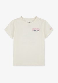 T-shirt en coton couleur crème à manches courtes, avec un logo "Converse Athletic Dept." rose et bleu sur la poitrine et des accents orange sur la manche.