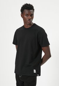 Camiseta negra de manga corta con cuello redondo, fabricada en tejido suave, con detalle de etiqueta en el lateral y un corte relajado.