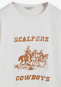 Camiseta de algodón blanca con un gráfico vintage de vaquero en naranja. El texto dice "SCALPERS COWBOYS" en letras bold y desgastadas.