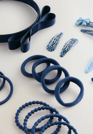 Accessoires capillaires bleu marine disposés sur une surface claire : un bandeau, des élastiques et des clips avec des textures et motifs variés.