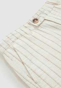 Bež kratke hlače iz teksturirane tkanine z tankimi horizontalnimi črtami in rjavim gumbom za zapiranje. Ima stranske žepe in našit pas.