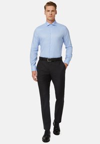Jasnoniebieska koszula z długim rękawem z guzikiem z przodu, zestawiona z czarnymi spodniami i wypolerowanymi czarnymi skórzanymi butami.