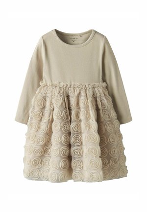 Cremefarbenes Langarmkleid mit einem gerippten Oberteil und einem Rüschenschnüffelrock, geschmückt mit Stoffrosenapplikationen, die ein strukturiertes Aussehen erzeugen.