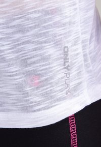 White, sheer sports top with a subtle texture; features "ONLY PLAY" branding. Paired with black pants accented by pink stitching.