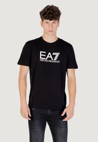 Camiseta de algodón negra con un logo gráfico blanco "EA7 EMPORIO ARMANI" en el frente. Mangas cortas, cuello redondo y dobladillo recto.