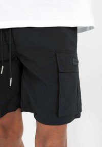 Černé cargo šortky z texturované látky, s boční kapsou, šňůrkovým zavíráním a značkovým štítkem na boku.
