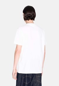 Weißes Baumwoll-T-Shirt mit Rundhalsausschnitt und kurzen Ärmeln, mit schlichtem Rückansicht, vor einem hellgrauen Hintergrund präsentiert.